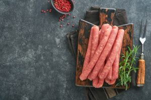 Meat beef sausages. Raw barbecue sausages with spices, vegetables and ingredients for cooking on bla
